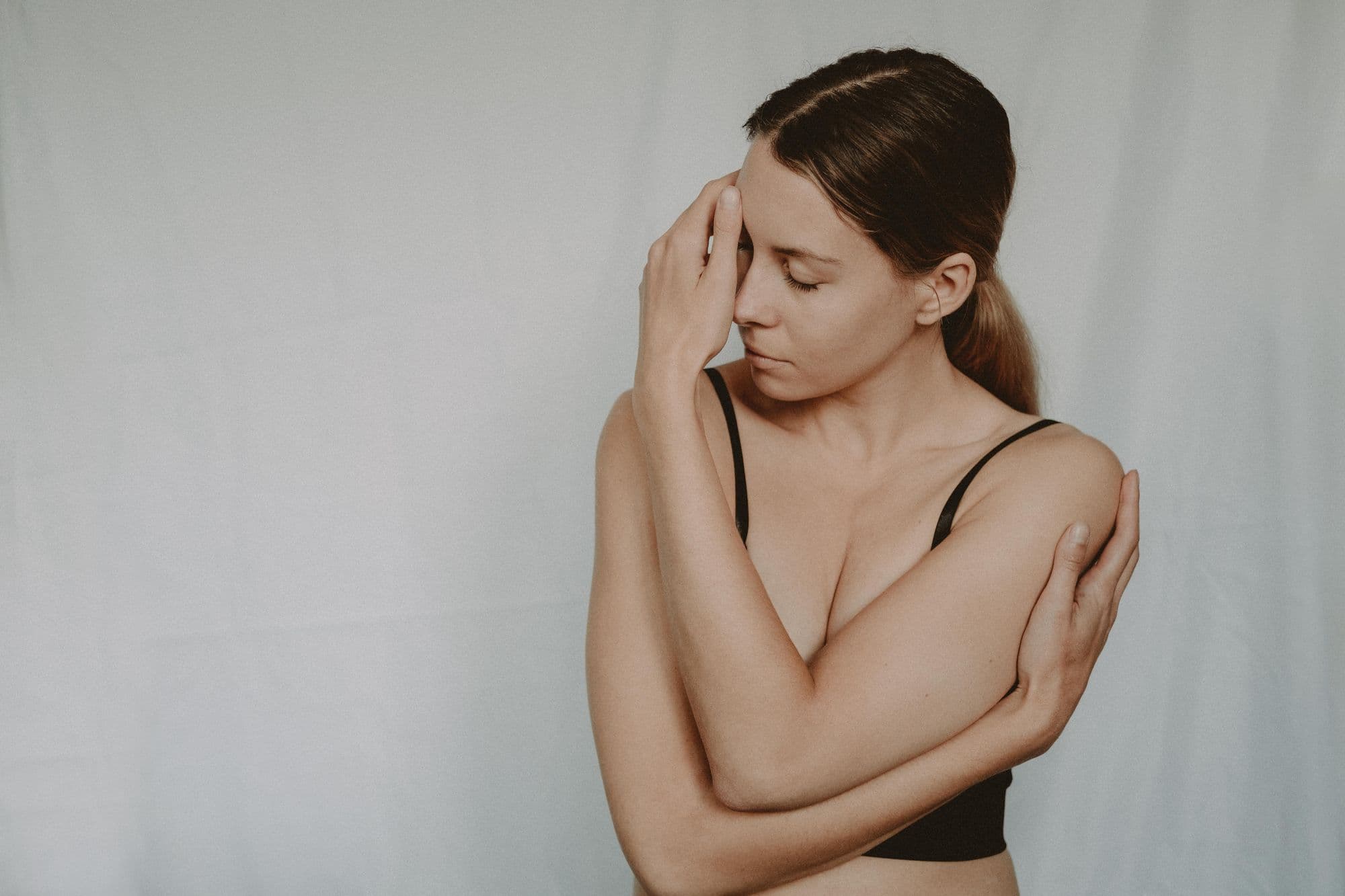 A woman thoughtfully holds her hand to her forehead, eyes closed.